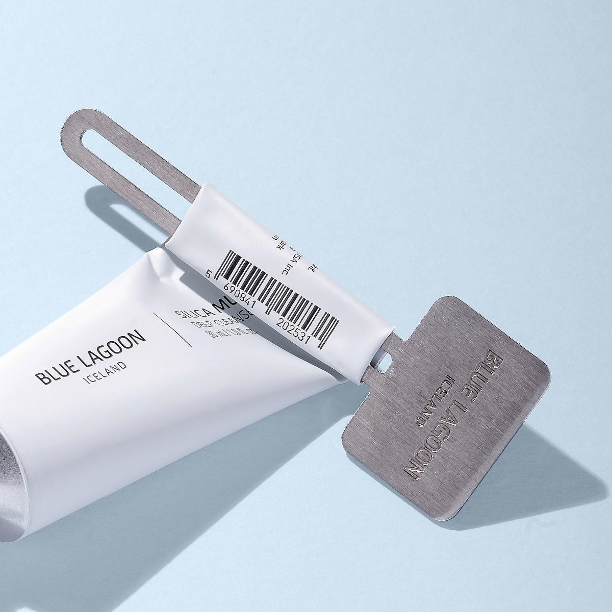 Tube/Mask Squeezer Key festur á ál-húðvörutúbu á ljósbláum bakgrunni